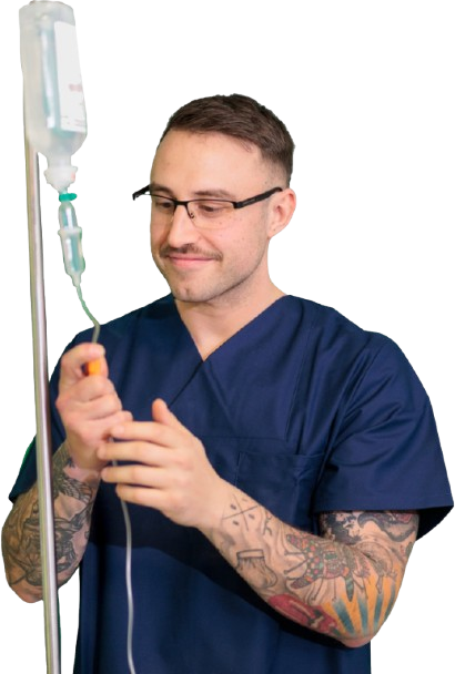 Person in dunkelblauer medizinischer Arbeitskleidung mit tätowierten Armen hält Infusionsständer mit Tropfbeutel und Schlauch.